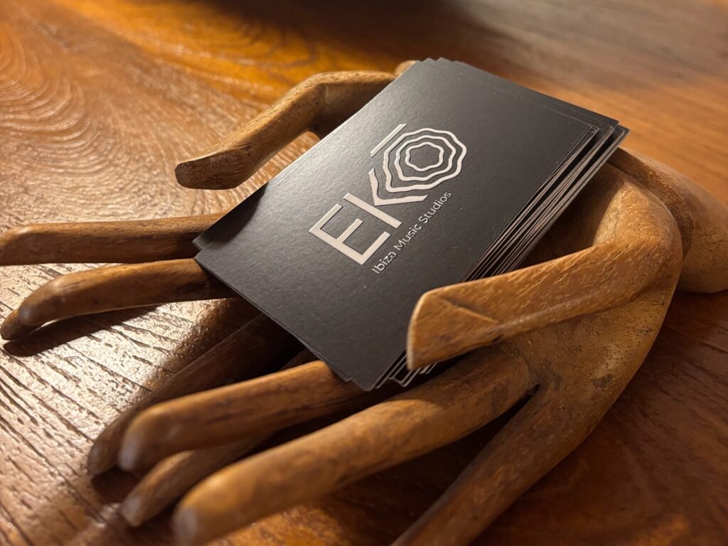 Two wooden hands hold contact cards for Ekō Studios Ibiza, a premier studio retreat in Spain and recording studio in Ibiza, on a rustic wooden table.